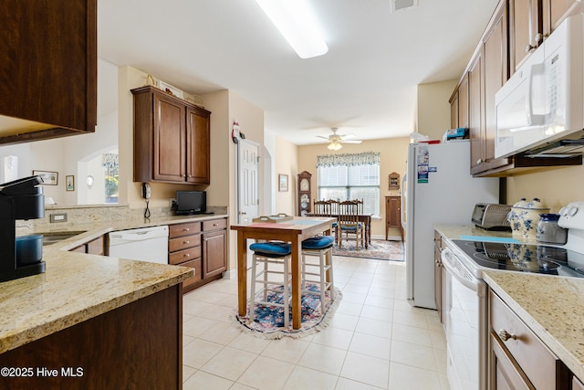 kitchen with ceiling fan, white appliances, light tile patterned flooring, and light stone countertops