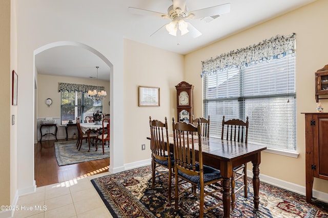 tiled dining room featuring ceiling fan with notable chandelier