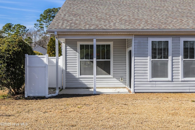 doorway to property featuring a yard, fence, and roof with shingles