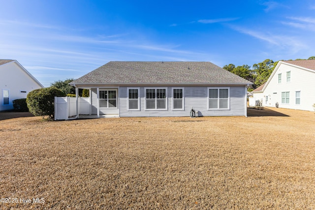 back of house featuring a shingled roof and a lawn