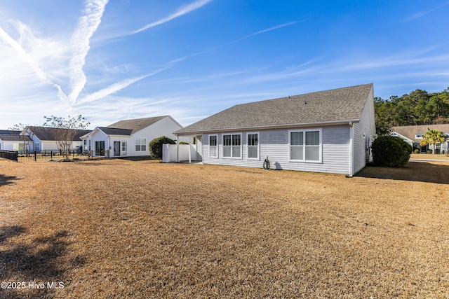 back of property featuring a shingled roof, fence, and a yard