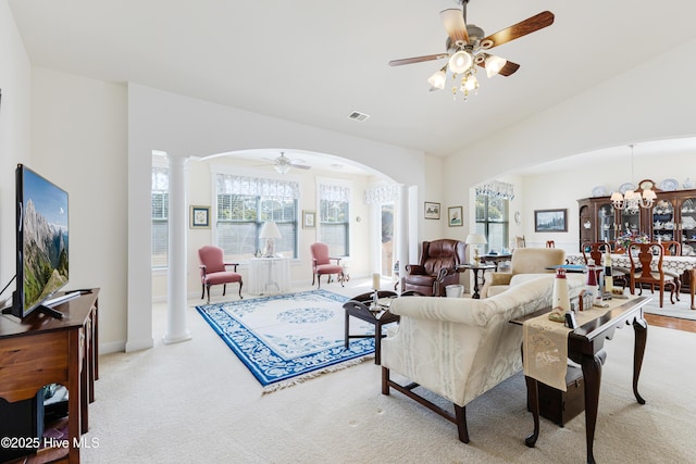 carpeted living area with arched walkways, ceiling fan with notable chandelier, visible vents, vaulted ceiling, and decorative columns