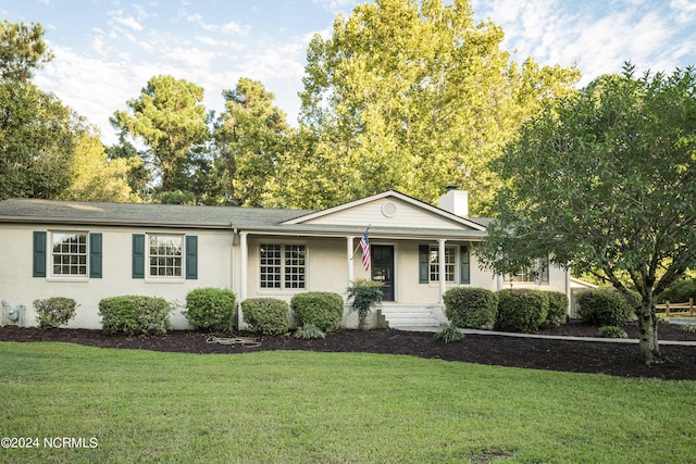 ranch-style home with a porch, a chimney, a front lawn, and brick siding