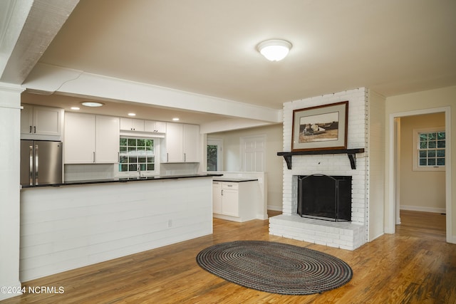 kitchen with a fireplace, a sink, wood finished floors, stainless steel refrigerator, and dark countertops