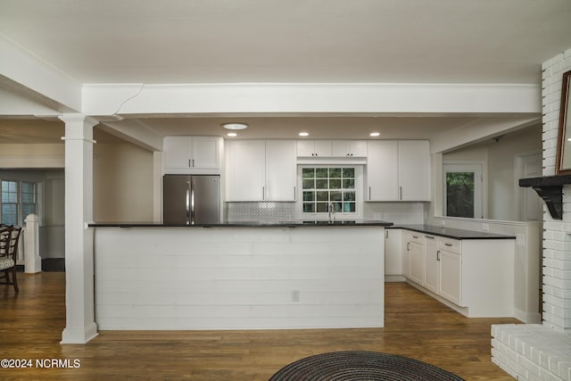 kitchen featuring tasteful backsplash, white cabinets, dark countertops, stainless steel refrigerator, and dark wood-style flooring