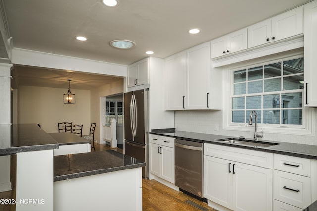 kitchen with appliances with stainless steel finishes, white cabinets, a sink, and wood finished floors