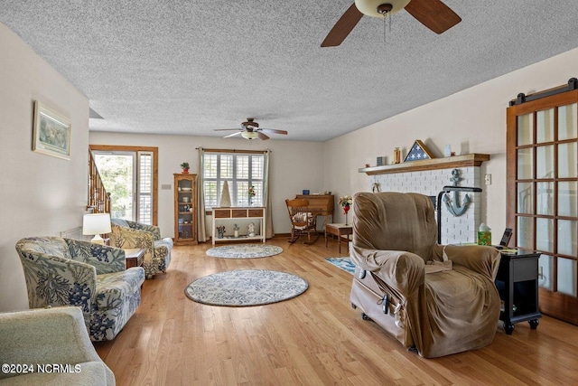 living room with a textured ceiling, ceiling fan, and light hardwood / wood-style floors