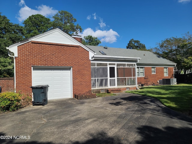 rear view of house with central air condition unit, a sunroom, a lawn, and a garage