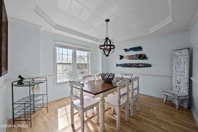 dining area featuring crown molding, a raised ceiling, light hardwood / wood-style flooring, and an inviting chandelier