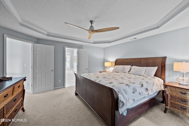 carpeted bedroom with a textured ceiling, a raised ceiling, ceiling fan, and ensuite bath