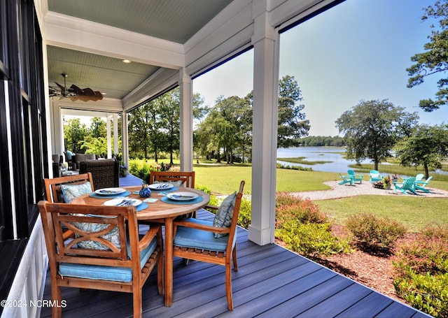 wooden terrace with ceiling fan, a yard, and a water view