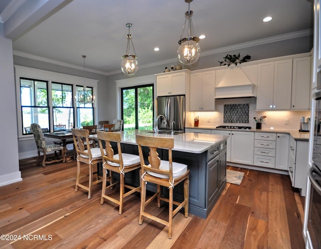 kitchen with stainless steel appliances, a center island with sink, white cabinetry, and premium range hood