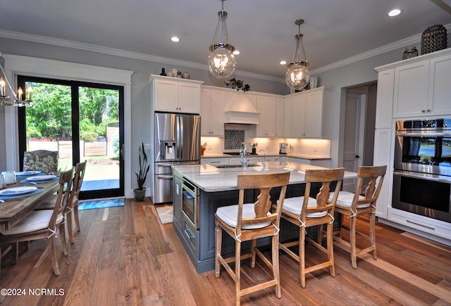 kitchen featuring white cabinetry, hanging light fixtures, a center island with sink, appliances with stainless steel finishes, and hardwood / wood-style flooring