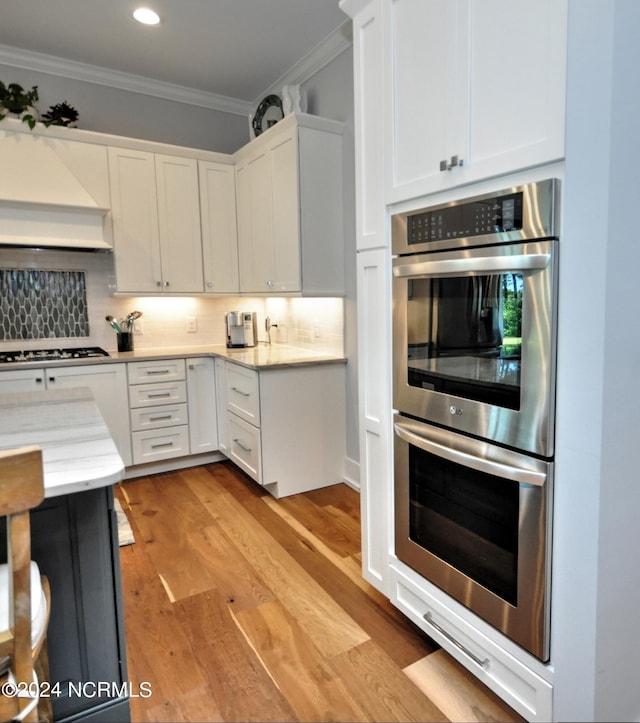 kitchen with gas cooktop, light wood-type flooring, stainless steel double oven, and white cabinetry