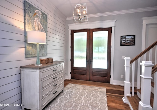 foyer with hardwood / wood-style floors, wood walls, an inviting chandelier, french doors, and ornamental molding