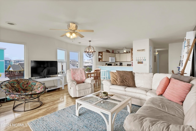 living room featuring light wood-style floors, visible vents, and ceiling fan with notable chandelier