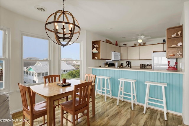 dining space with light wood-style floors, baseboards, visible vents, and ceiling fan with notable chandelier