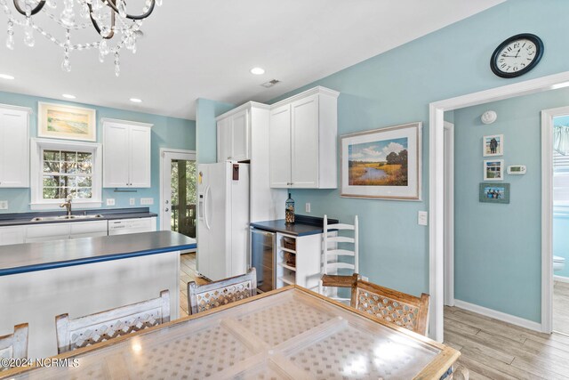 kitchen with white cabinets, light wood-type flooring, white fridge with ice dispenser, sink, and a notable chandelier