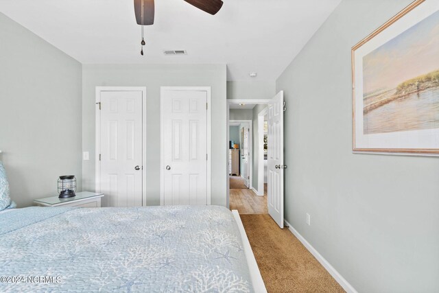 bedroom featuring ceiling fan, light colored carpet, and two closets