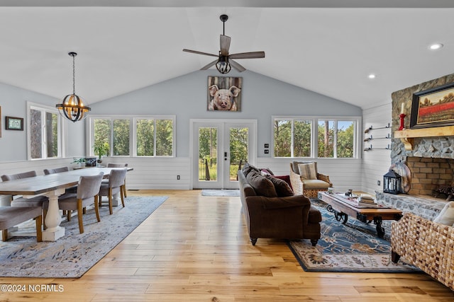 living room featuring ceiling fan with notable chandelier, light hardwood / wood-style flooring, wood walls, and french doors