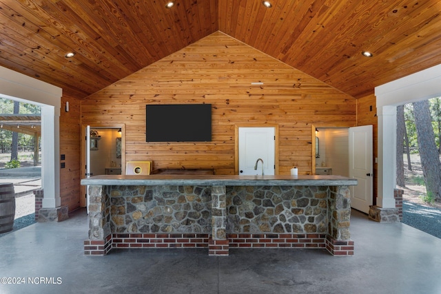 bar featuring wooden walls, concrete flooring, and high vaulted ceiling