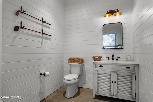 bathroom with wooden walls, vanity, and toilet