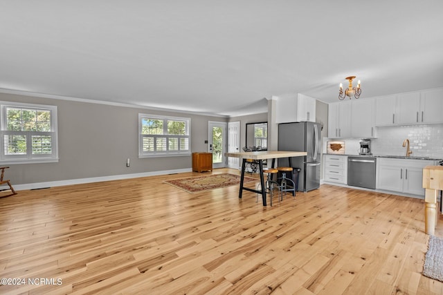 kitchen featuring white cabinets, appliances with stainless steel finishes, a notable chandelier, light hardwood / wood-style floors, and backsplash