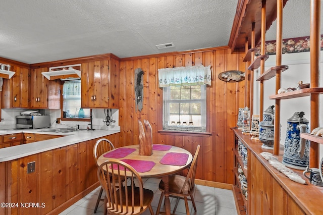 kitchen featuring wood walls, a wealth of natural light, a textured ceiling, and light tile patterned flooring