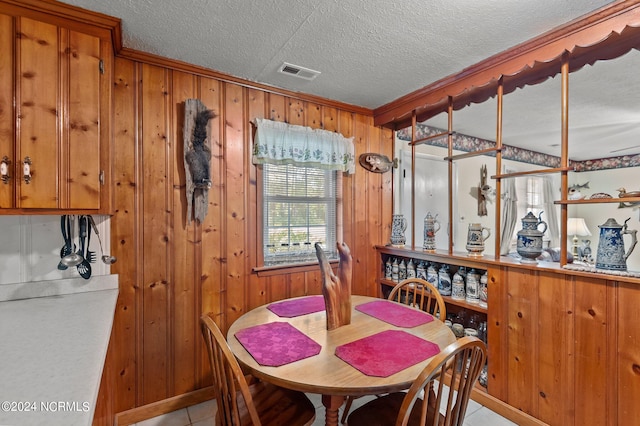 tiled dining area featuring wooden walls, a textured ceiling, and ornamental molding