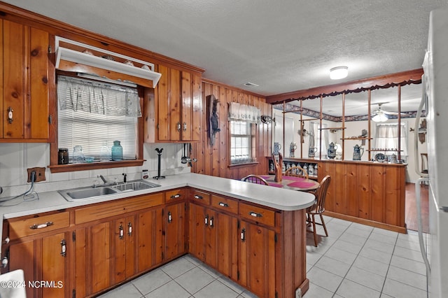 kitchen featuring a textured ceiling, light tile patterned floors, kitchen peninsula, sink, and ceiling fan