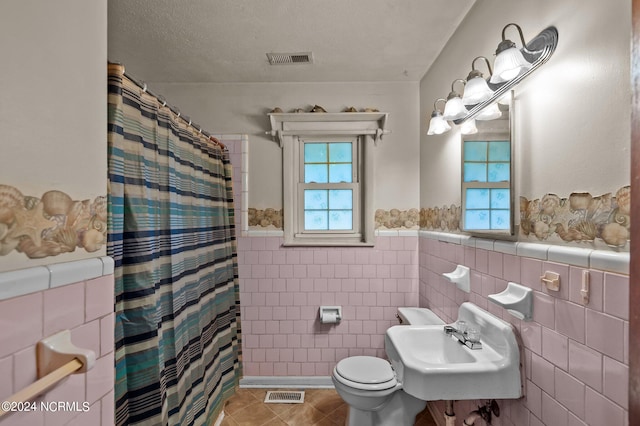 bathroom featuring toilet, a textured ceiling, backsplash, sink, and tile walls