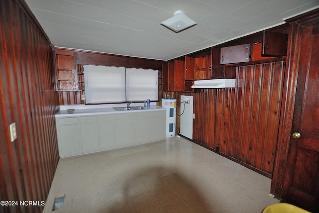 kitchen featuring under cabinet range hood, wood walls, a sink, water heater, and light floors