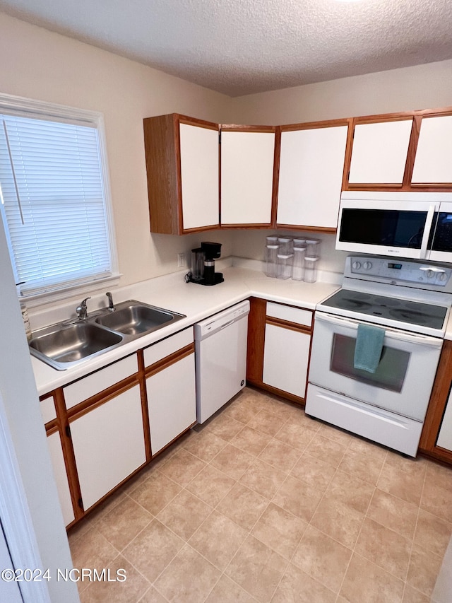 kitchen with a textured ceiling, sink, white appliances, and white cabinets