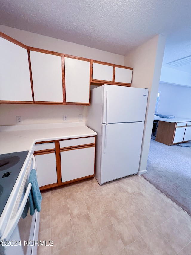 kitchen with a textured ceiling, white fridge, range with electric stovetop, light carpet, and white cabinets