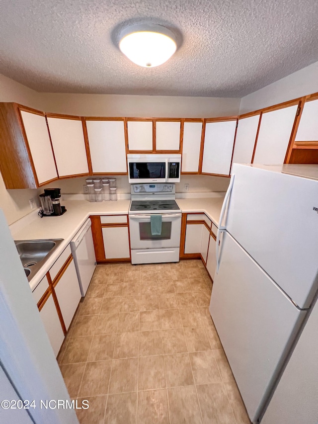 kitchen with white appliances, sink, white cabinets, and a textured ceiling