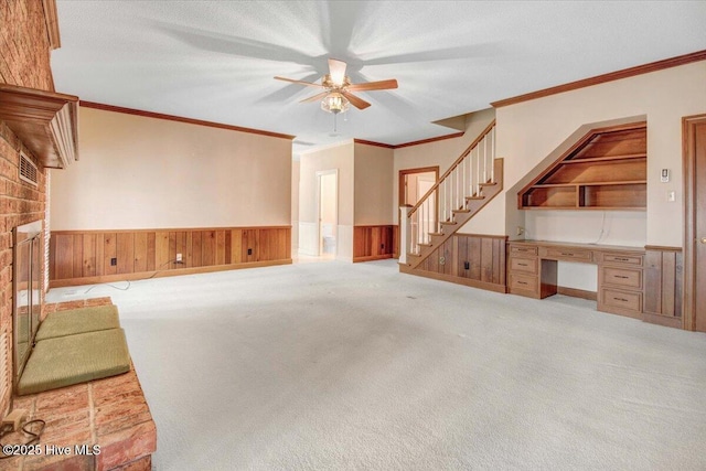 unfurnished living room featuring built in features, built in desk, a brick fireplace, light colored carpet, and wood walls