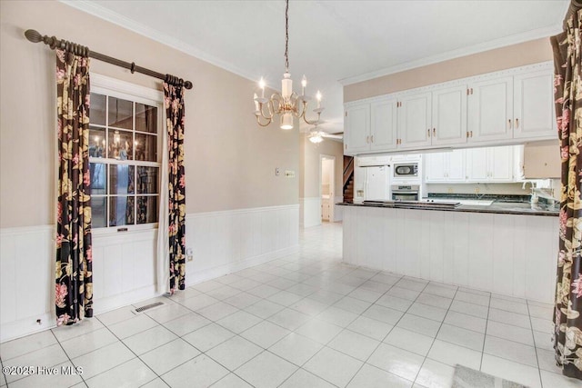 kitchen with hanging light fixtures, ornamental molding, white cabinets, and appliances with stainless steel finishes