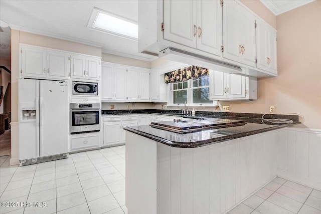 kitchen featuring appliances with stainless steel finishes, white cabinetry, ornamental molding, light tile patterned floors, and kitchen peninsula