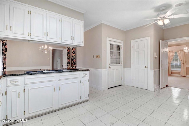 kitchen featuring light tile patterned flooring, ceiling fan with notable chandelier, white cabinets, dark stone counters, and crown molding