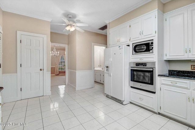 kitchen with light tile patterned floors, stainless steel appliances, ornamental molding, white cabinets, and ceiling fan with notable chandelier