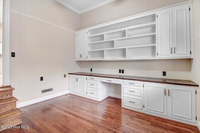 unfurnished office featuring crown molding, built in desk, and light wood-type flooring