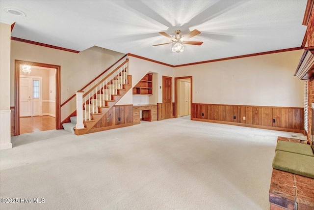 unfurnished living room featuring wooden walls, ornamental molding, ceiling fan, and carpet