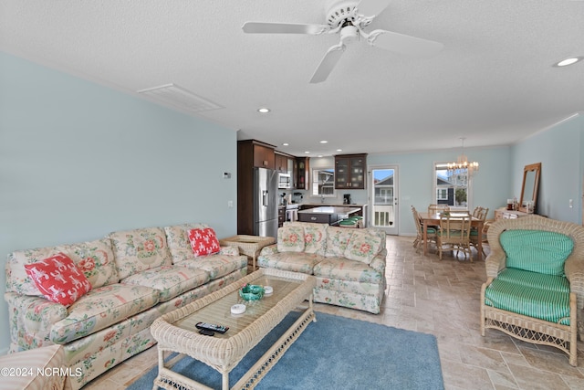 living room featuring a textured ceiling and ceiling fan with notable chandelier