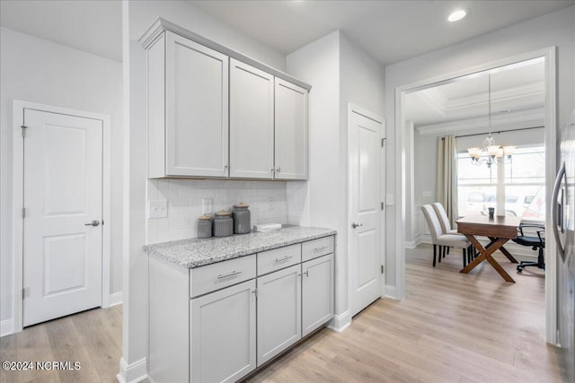 kitchen featuring light stone countertops, backsplash, a chandelier, and light hardwood / wood-style floors