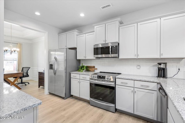 kitchen featuring an inviting chandelier, light hardwood / wood-style flooring, appliances with stainless steel finishes, white cabinetry, and light stone counters