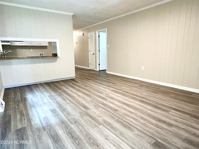 unfurnished living room with sink, wood walls, light hardwood / wood-style floors, and crown molding