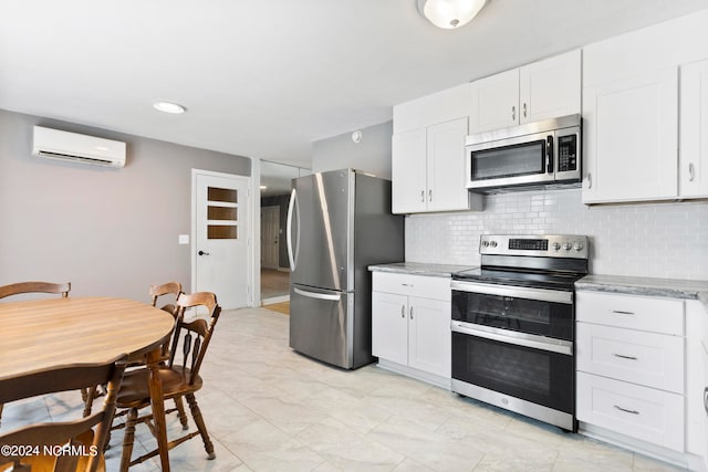 kitchen with a wall unit AC, white cabinetry, tasteful backsplash, stainless steel appliances, and light stone countertops