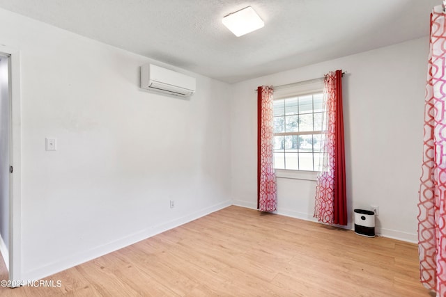 unfurnished room featuring a wall unit AC, a textured ceiling, and light hardwood / wood-style flooring