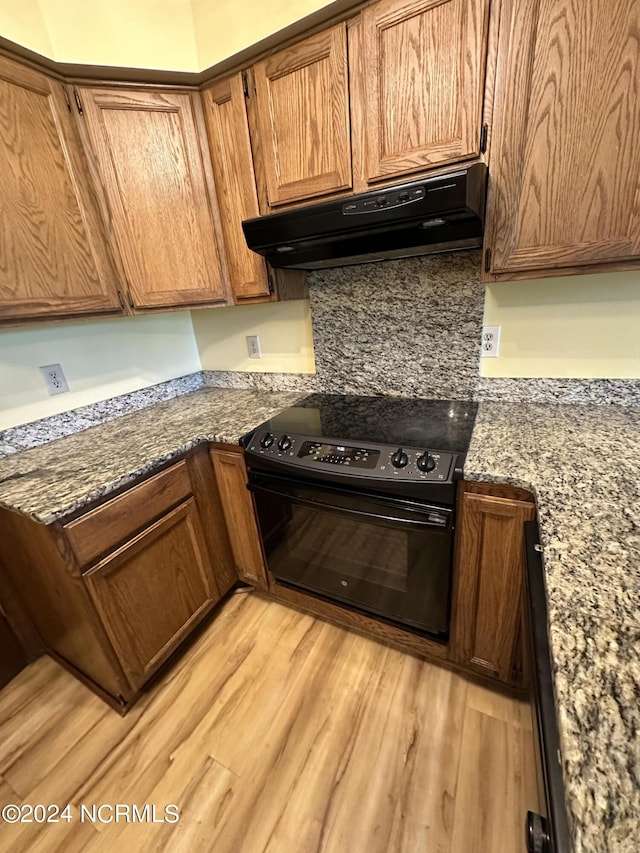 kitchen featuring black electric range, brown cabinets, light wood-style floors, stone countertops, and under cabinet range hood