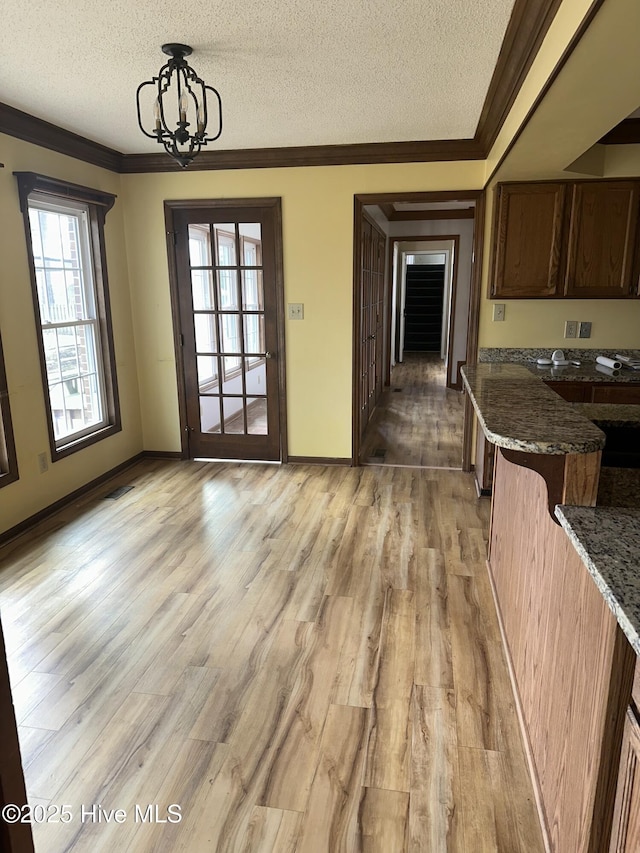 unfurnished dining area with baseboards, light wood-style flooring, ornamental molding, an inviting chandelier, and a textured ceiling